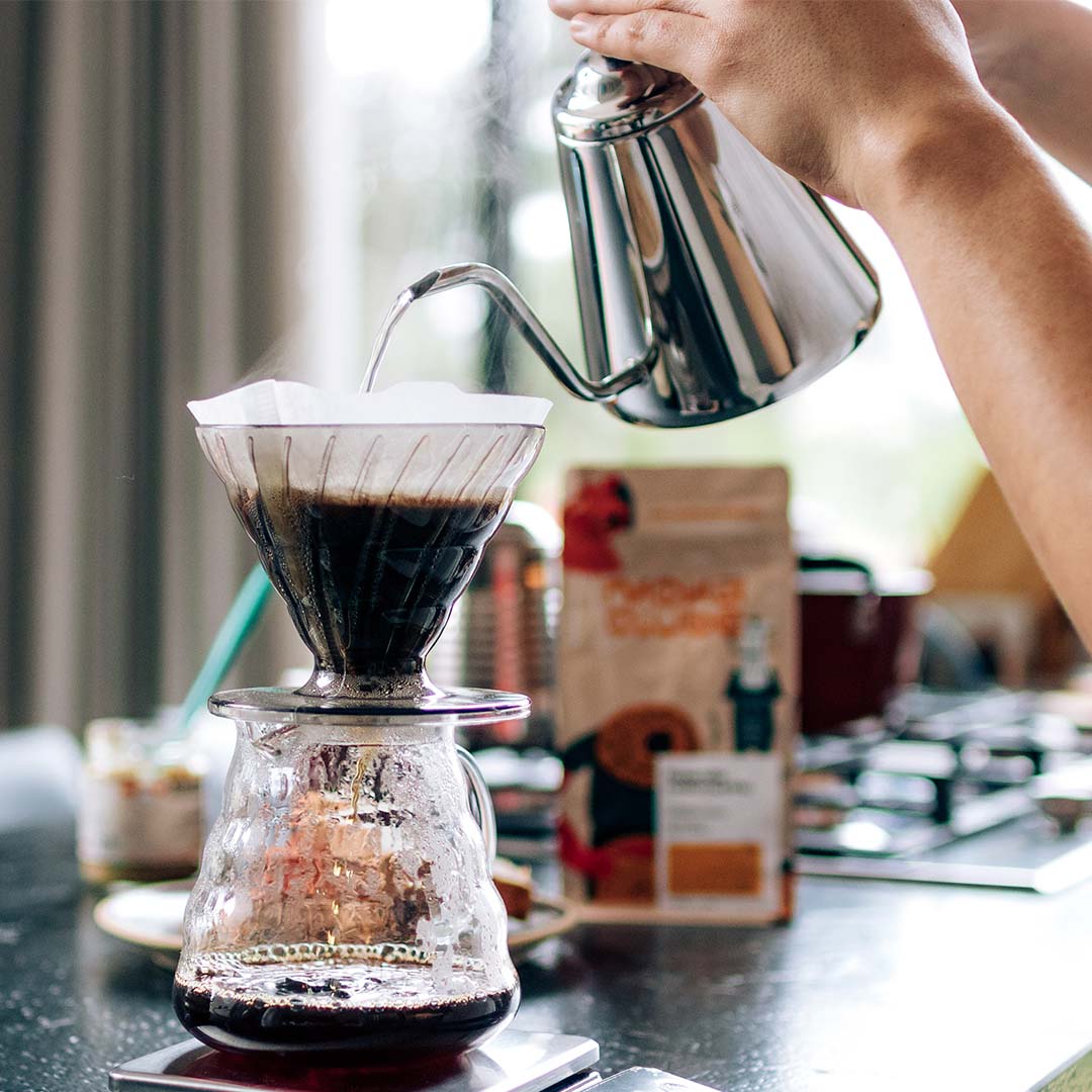 Chaleira bico de ganso jogando água em filtro v60 para preparar café