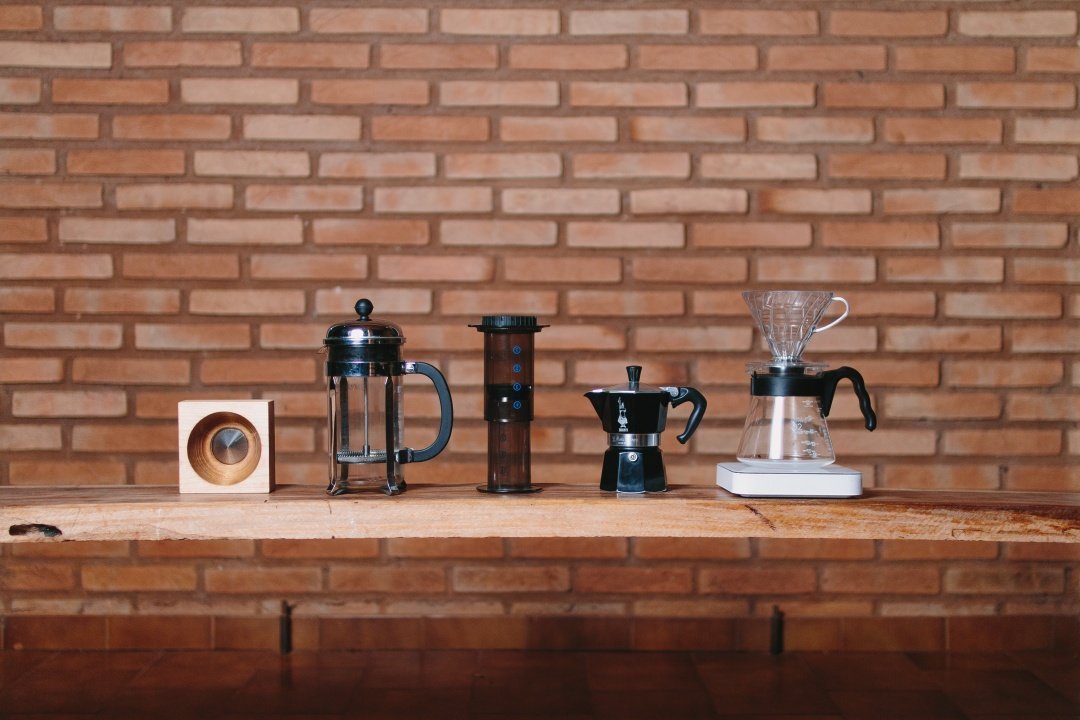 diversos métodos de extração de café alinhados em uma parede de tijolo