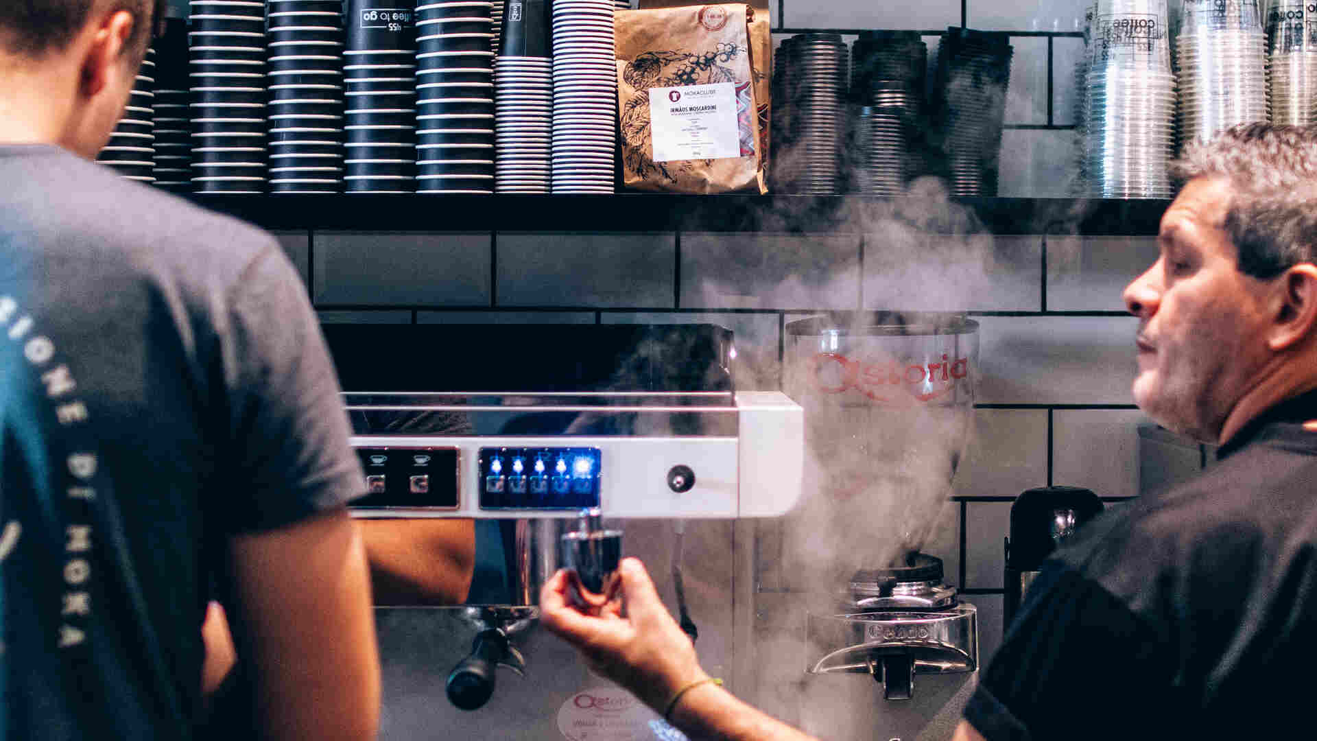 vapor saindo de máquina de expresso com dois homens operando