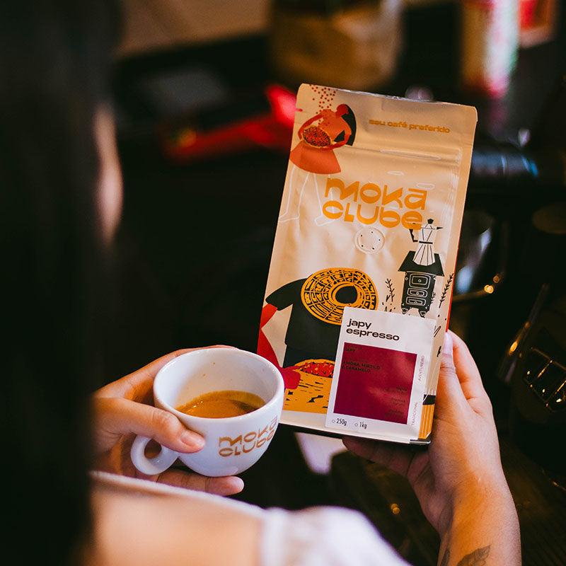 Mulher segurando um pacote do café Japy Espresso e uma xicara de café