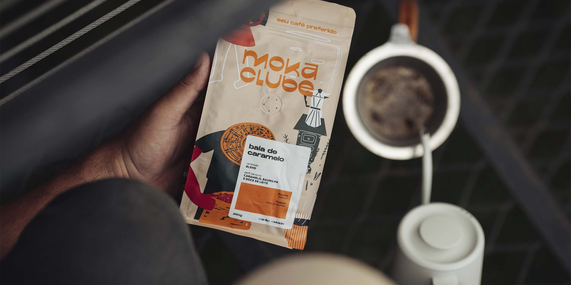 Mão segurando pacote de café bala caramelo com café sendo passado no chão