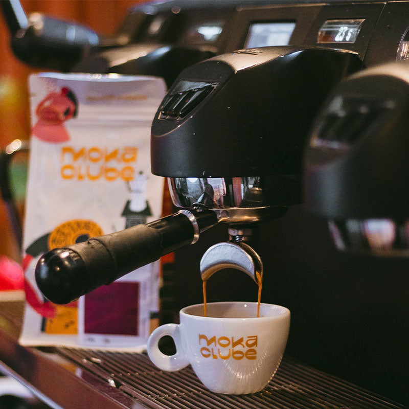 Uma maquina de café extraindo um espresso ao fundo pacote do café japy espresso