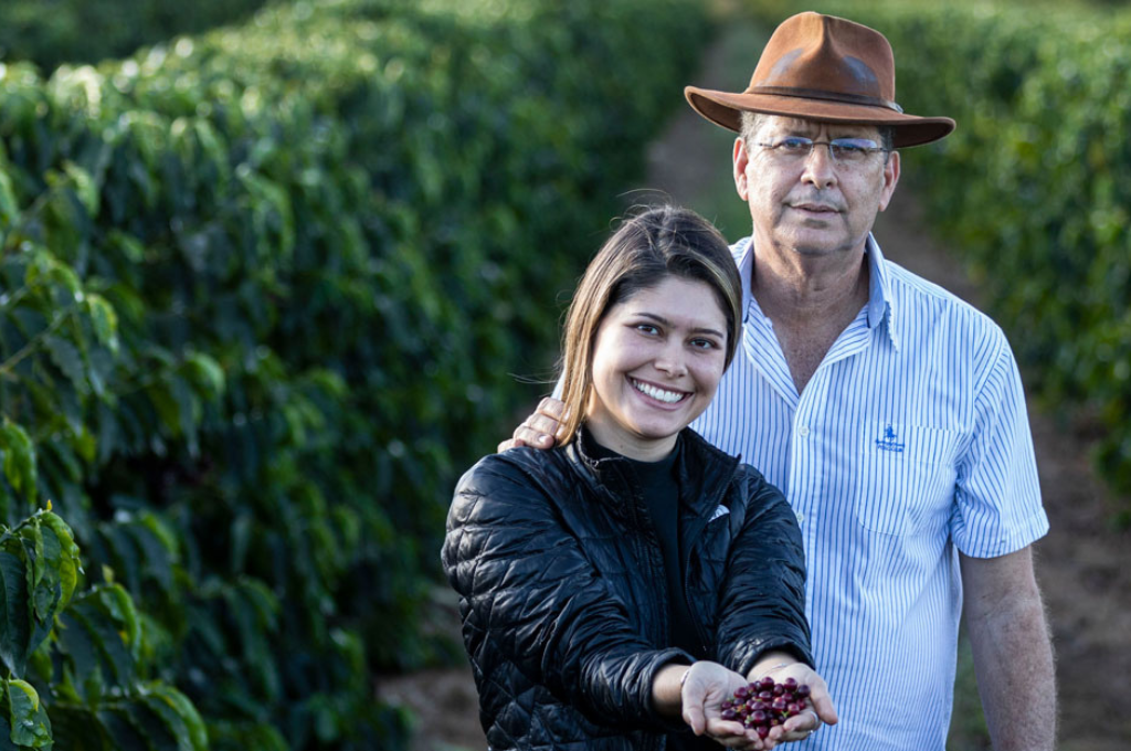 Mulher segurando frutos de café junto de homem na plantação