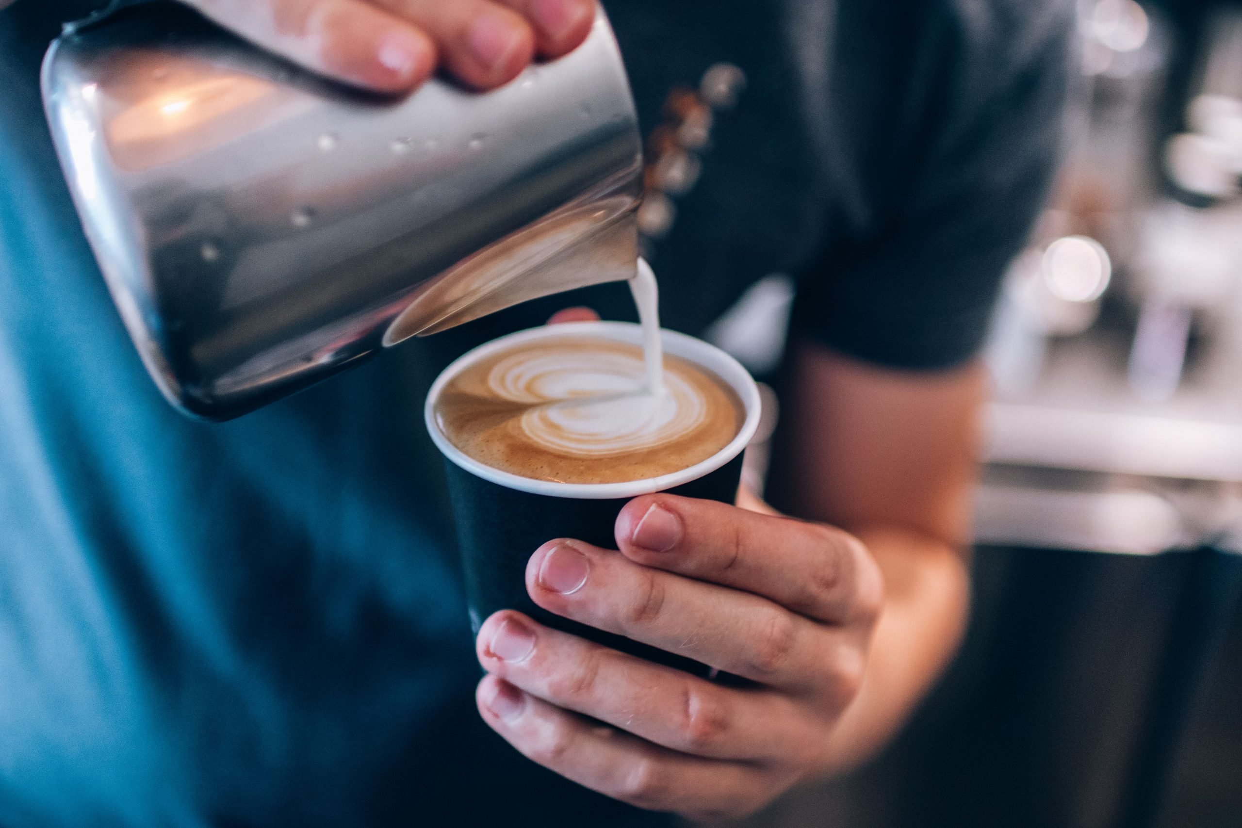 Homem depositando leite vaporizado na xícara de café.