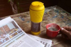 Cafeteira pressca amarela em cima de uma mesa com jornal aberto.