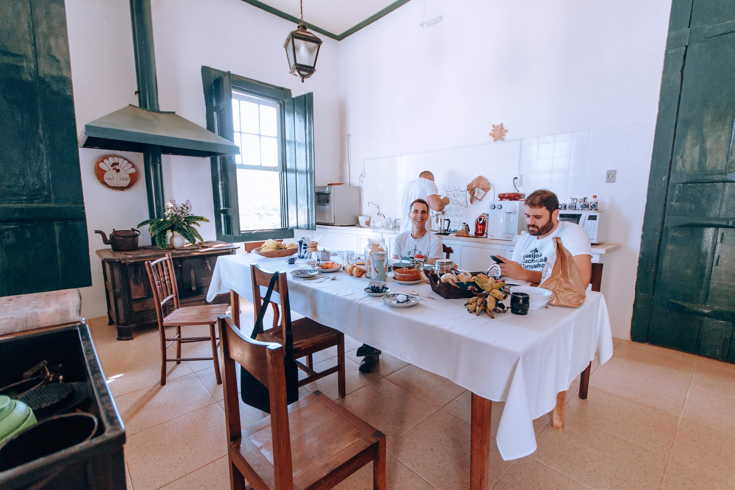 Mesa cheia de comidas com duas pessoas sentadas nas cadeiras em volta.