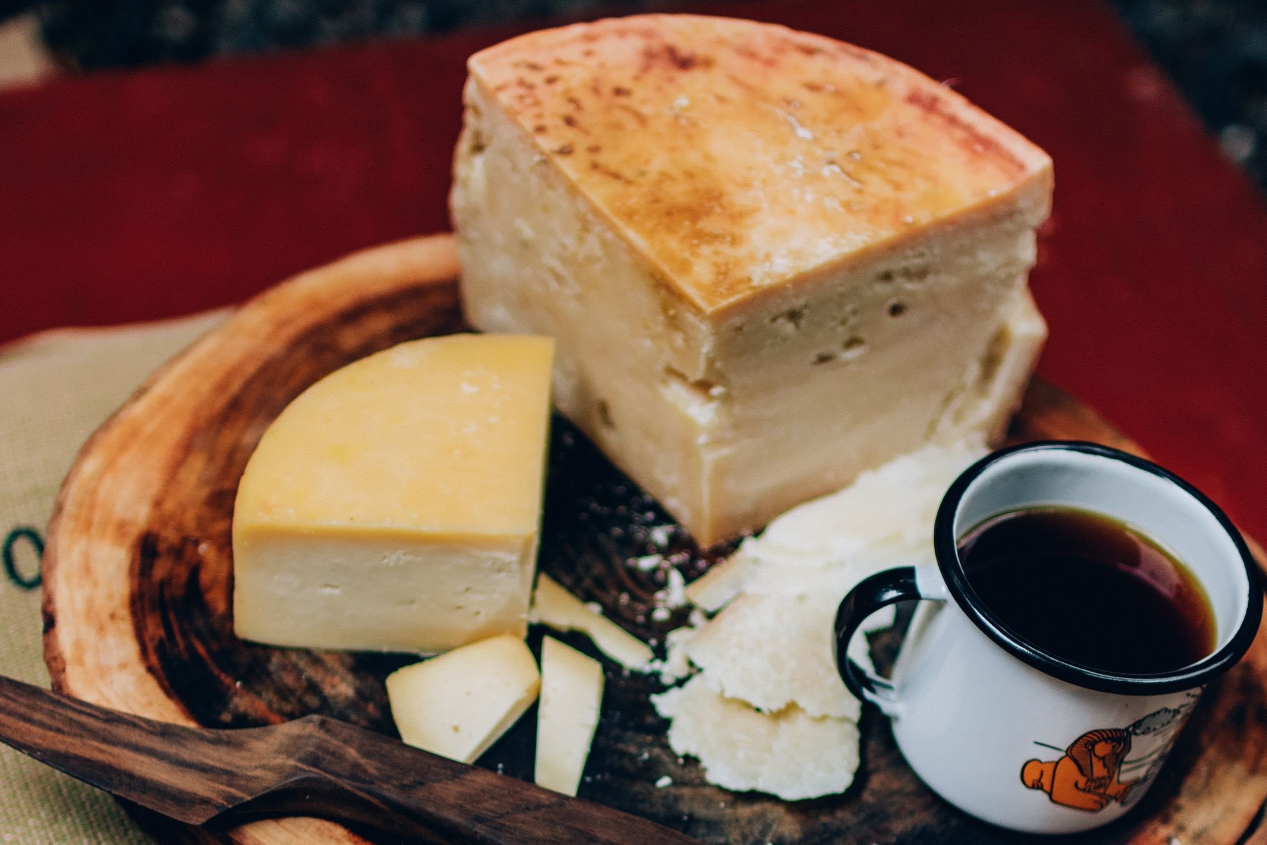 Mesa com queijo cortado aos pedaços e uma xícara cheia de café.