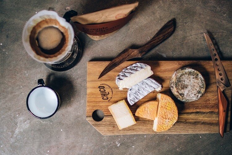 Tábua com queijos e uma xícara de café ao lado.