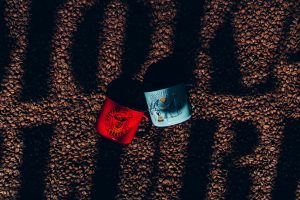 Canecas colocadas sobre grãos de café com a escrita Moka Clube sobre eles em uma espécie de sombra,