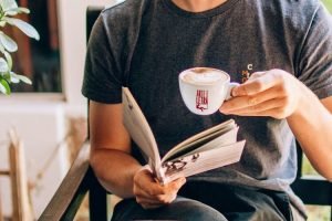 Homem lendo com uma xícara de café na mão.