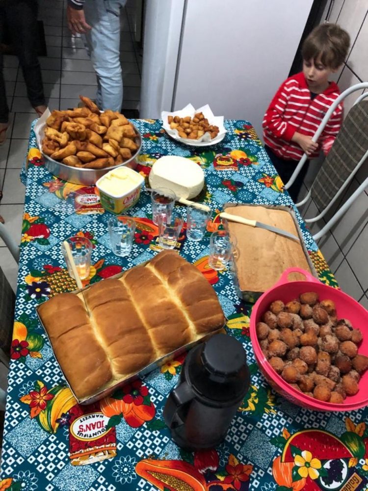 Mesa de cozinha com pães, salgadinhos, queijo e cafeteira.