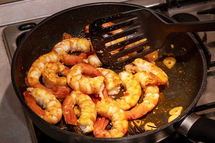 Camarões em uma frigideira e uma espátula mexendo na comida.